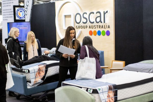 Oscar Group Australia exhibitor staff demonstrating a gallery of accessible beds on display at ATSA Melbourne 2021