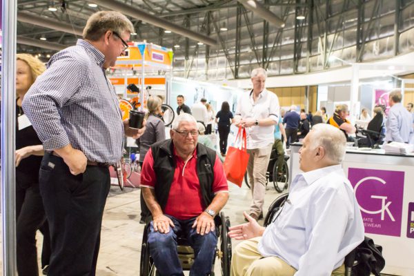 A photo of a group of men around each other talking at the Sydney Expo 2019 event. Two men are wheelchair uses, once man is standing.