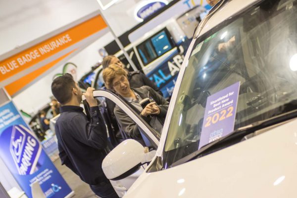 An exhibitor showcasing an accessible vehicle to a visitor on the expo floor